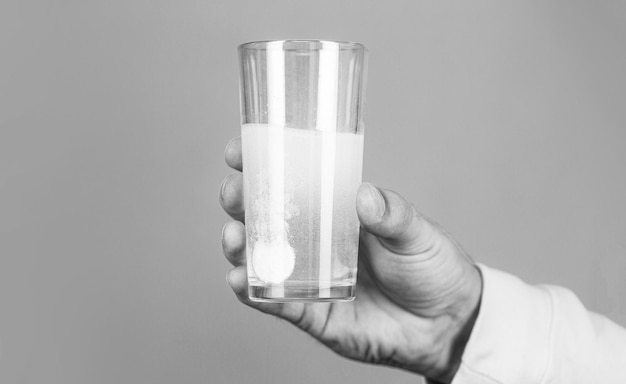 Píldora blanca y un vaso de agua en las manos del hombre Concepto de salud Primer plano del hombre que sostiene una píldora