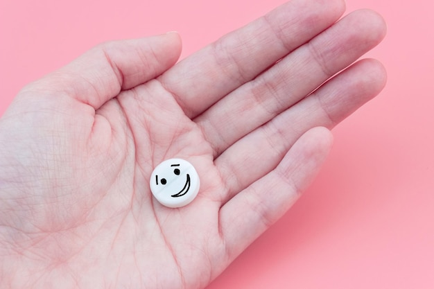 Píldora con un emoticono en la mano sobre un fondo rosa Tratamiento y prevención de la salud