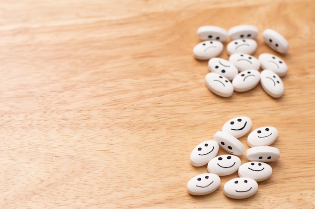 Píldora de medicina con caras felices y tristes sobre una mesa de madera con espacio para copiar