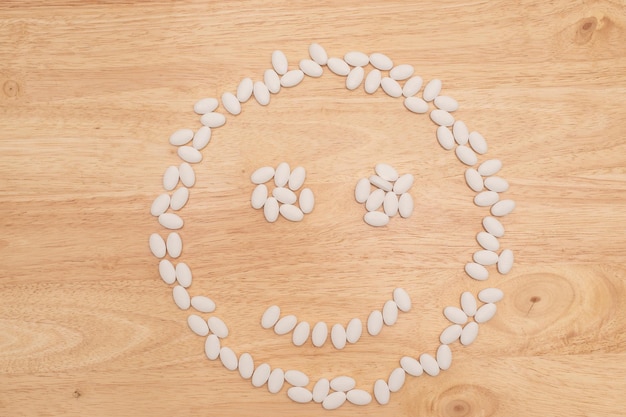 Píldora de medicina en la mesa con forma de cara feliz en el fondo de madera