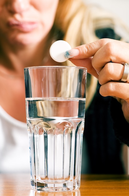 Foto píldora sostenida sobre un vaso de agua