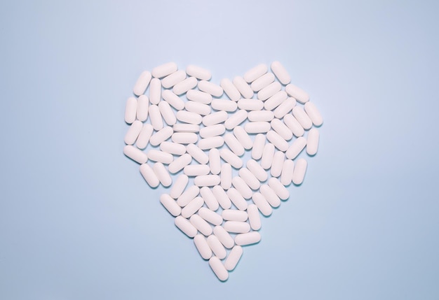 Píldoras blancas en forma de corazón y frasco blanco sobre fondo azul. Pastillas para la salud del corazón.