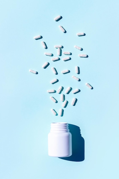 Píldoras blancas en forma de corazón salen volando de la botella sobre fondo azul Medicina concepto de atención médica Vista superior Lay Flat
