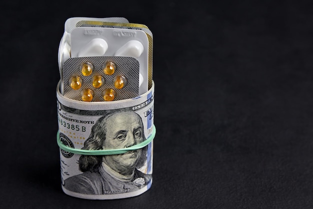 Las píldoras en blísteres se envuelven con billetes de dólar sujetos con una banda elástica sobre un fondo de hormigón negro
