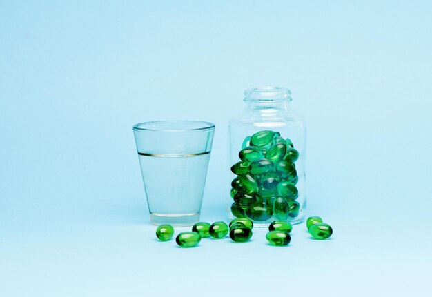 Píldoras de cápsulas médicas y agua de vidrio sobre un fondo azul.
