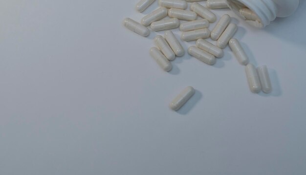 Píldoras y cápsulas médicas que se derraman de la botella en el fondo blanco