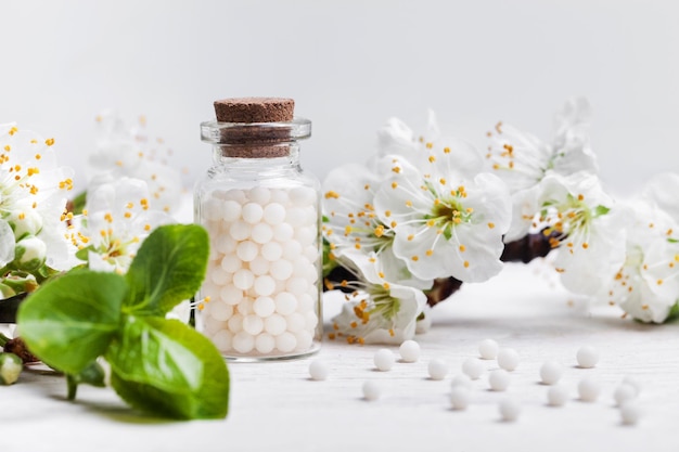 Píldoras homeopáticas con flores de primavera sobre fondo blanco de madera