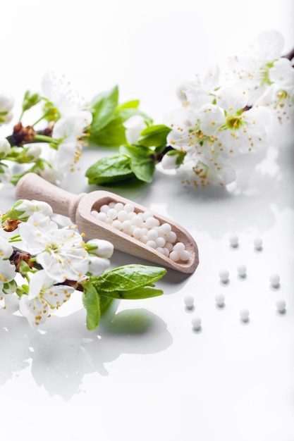 Píldoras homeopáticas con flores de primavera sobre fondo blanco de madera