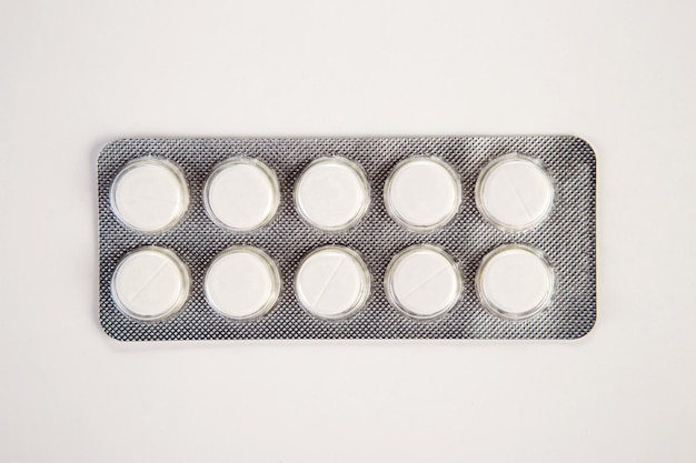 Píldoras médicas blancas en blister de plata sobre fondo blanco.