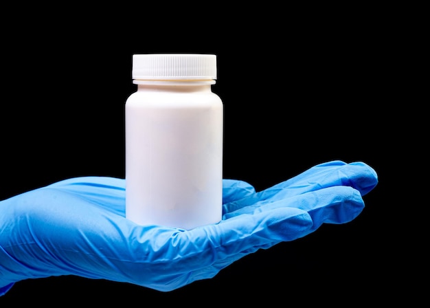 Píldoras médicas en frasco blanco sobre un fondo negro aislado con reflejo en la mano