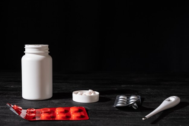 Foto píldoras médicas y termómetro en superficie de madera negra. concepto de autotratamiento: imagen minimalista de bajo perfil de medicamentos recetados.