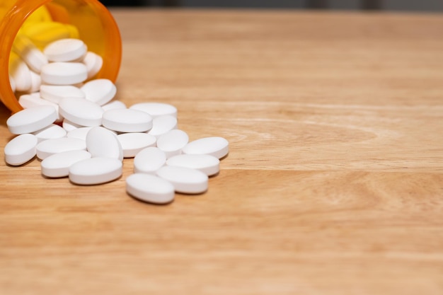 Píldoras de medicina saliendo de una botella naranja sobre una mesa