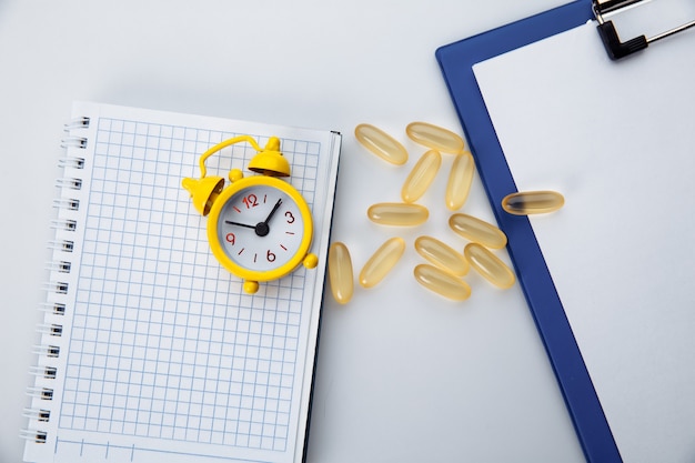 Píldoras de Omega 3 y reloj despertador en la mesa del médico blanco, concepto de salud