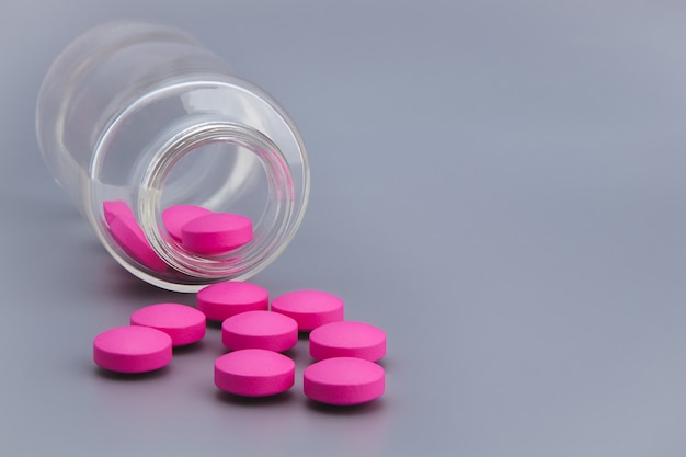 Las píldoras rosadas se esparcen desde una botella de vidrio sobre un gris.