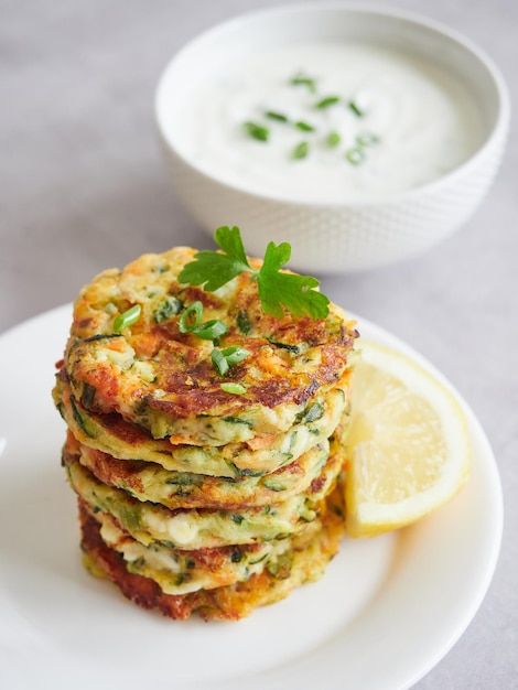 Pilha de bolinhos vegetarianos ou costeletas de legumes de abobrinha abobrinha com ervas frescas por cima Limão e tigela de molho de iogurte como guarnição