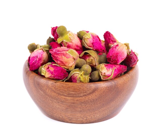 Pilha de botões secos de rosas de chá em uma tigela de madeira, isolados no fundo branco, caminho de recorte de chá de flor rosa