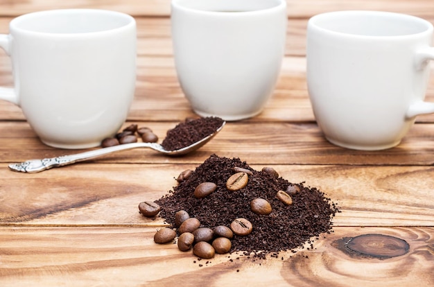 Pilha de café moído e grãos de café com xícaras e colher na mesa de madeira