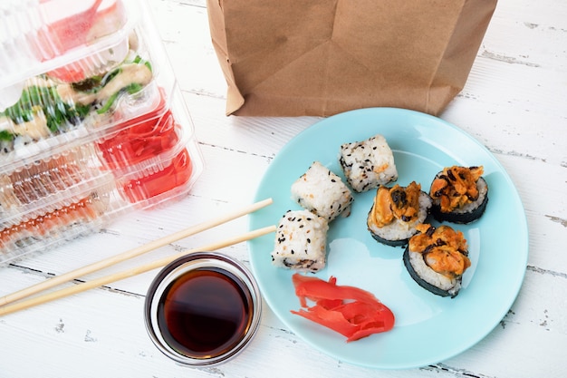 Pilha de caixas de plástico com conjuntos de rolo de sushi, prato com rolos e saco de papel. Entrega de alimentos