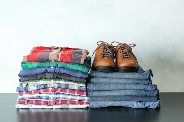 Pilha de camisas coloridas, jeans e sapatos na mesa contra a luz de fundo, espaço para texto