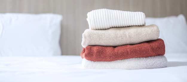 Pilha de camisolas de lã bege na cama no hotel de luxo ou resort ou casa. Relaxe, roupas de outono ou inverno, conceitos de lavanderia e férias