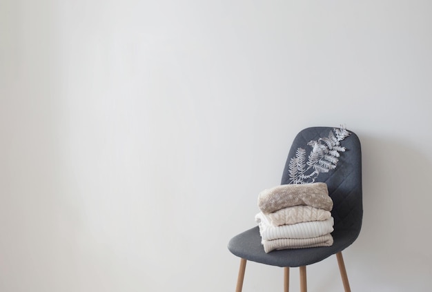 Pilha de camisolas na cadeira moderna cinza no quarto branco
