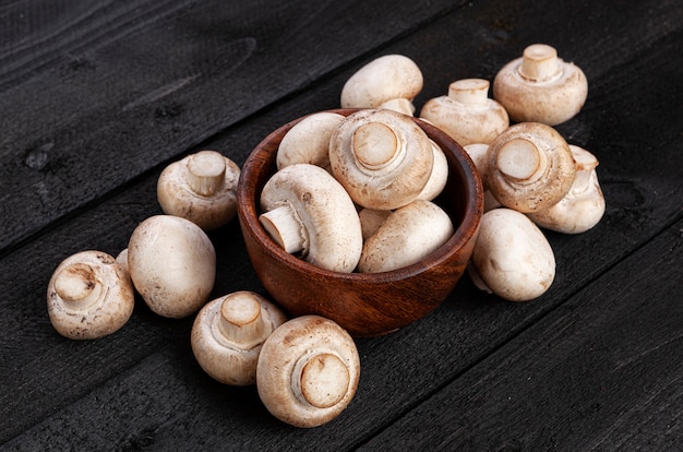 Pilha de cogumelos, champignon em uma tigela de madeira com fundo preto, vista superior