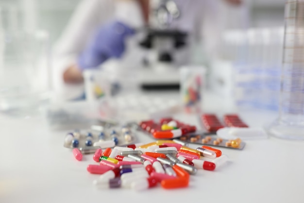 Pilha de comprimidos espalhados na mesa branca contra mulher fazendo pesquisa com medicina de microscópio