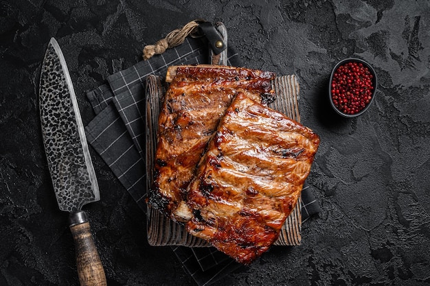 Foto pilha de costelas de porco grelhadas em molho de churrasco em uma tábua de cortar fundo preto vista superior