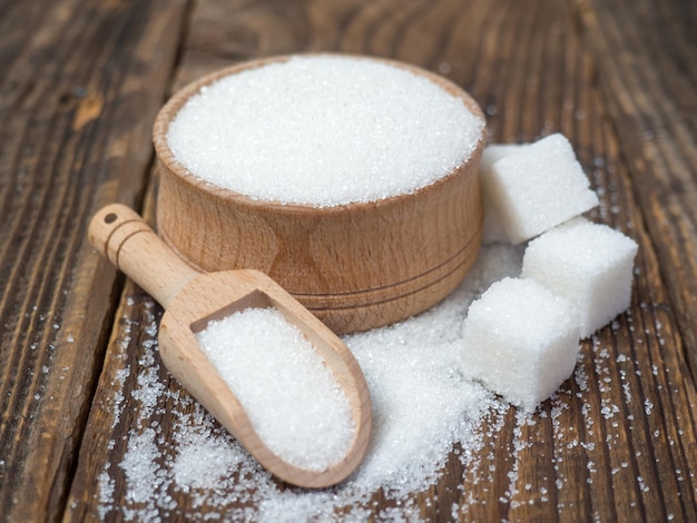 Pilha de cubos de açúcar e açúcar granulado em uma colher de madeira