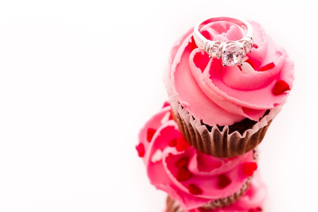 Pilha de cupcakes rosa com anel de noivado no topo.