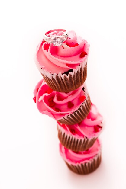 Pilha de cupcakes rosa com anel de noivado no topo.