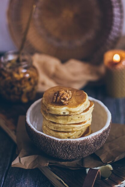 Pilha de deliciosas panquecas com mel, nozes em fundo de madeira