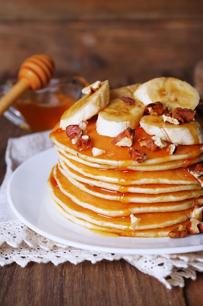 Pilha de deliciosas panquecas com nozes de mel de chocolate e fatias de banana no prato e guardanapo em fundo de madeira