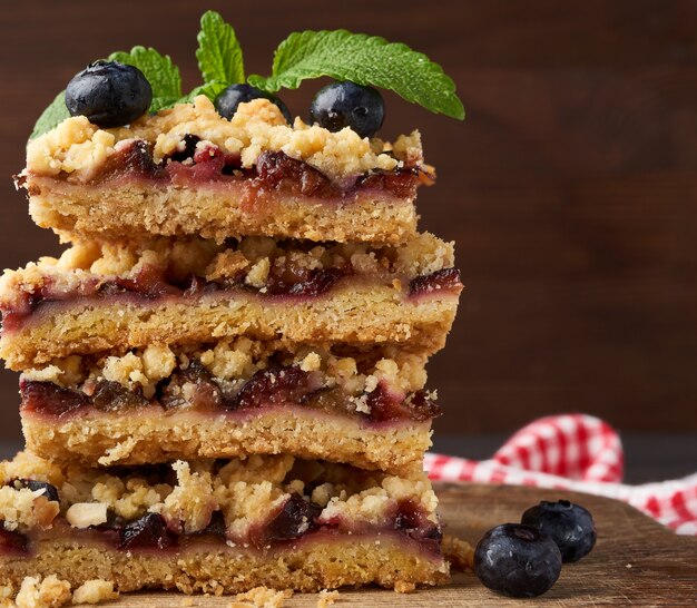 Pilha de fatias quadradas de torta crumble assada com ameixa azul em uma placa de madeira