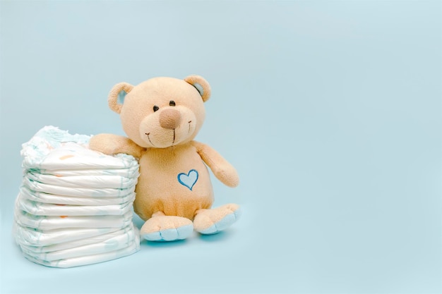 Pilha de fraldas com brinquedo de ursinho fofo na mesa posta para menina recém-nascida para chá de bebê presente presente em fundo azul com espaço de cópia Conceito de higiene médica de saúde