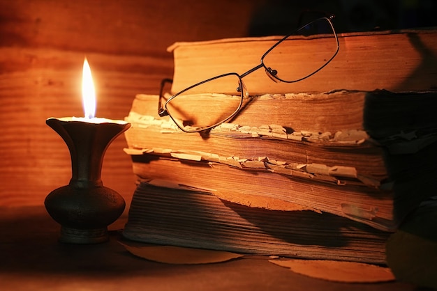 Pilha de livro velho e esfarrapado em uma mesa de madeira com velas e velas acesas