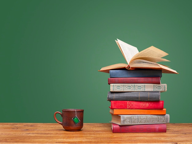 pilha de livros e uma xícara de chá em uma mesa de madeira sobre um fundo verde