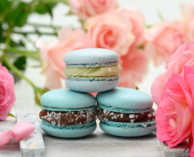 Pilha de macarons azuis em uma mesa branca e botões de rosa rosa, sobremesa deliciosa