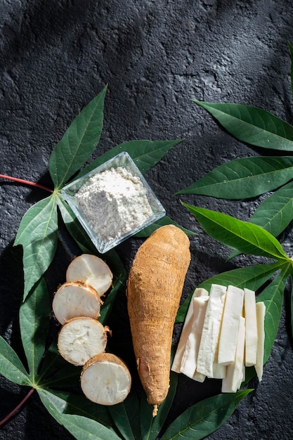 Pilha de mandioca e farinha de mandioca sobre fundo de textura rústica e escura Manihot esculenta