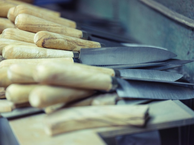 Pilha de novas facas de aço com cabos de madeira colocadas na bancada na oficina de ferreiro profissional