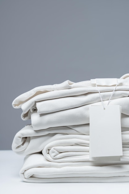 Pilha de novas roupas brancas com uma etiqueta de vestuário em branco sobre fundo cinza