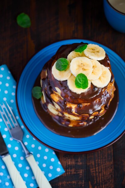 Pilha de panquecas com banana e chocolate em uma mesa de madeira escura