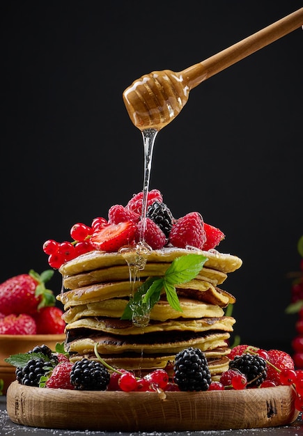 Pilha de panquecas com frutas frescas polvilhadas com mel em um fundo preto