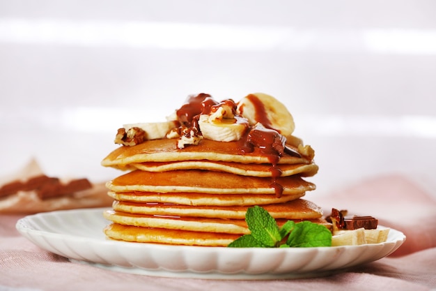 Pilha de panquecas com hortelã, nozes, chocolate e rodelas de banana na mesa com tecido