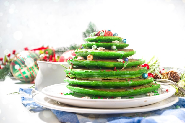 Pilha de panquecas de café da manhã de cor verde, como árvore de Natal com granulado de açúcar. Café da manhã festivo de Natal na mesa decorada de Natal e Ano Novo