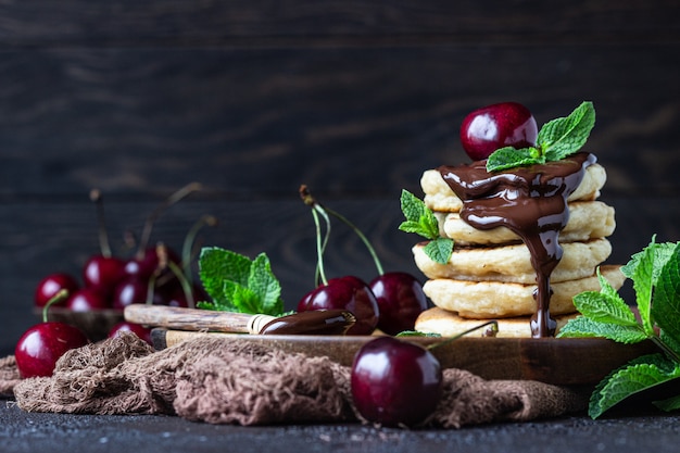 Pilha de panquecas macias ou bolinhos com geléia de chocolate e cereja, cereja fresca e hortelã.