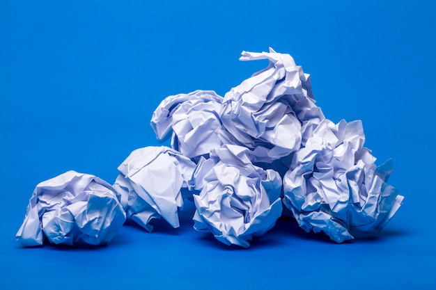 Pilha de pedaços de papel brancos enrugados sobre um fundo azul.