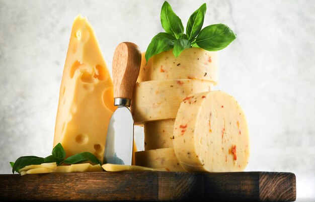 Pilha de queijo com tomate e tempero e queijo suíço com manjericão e faca na tábua de servir no fundo da mesa cinza claro Variedade de diferentes tipos de queijo Fundo de queijo