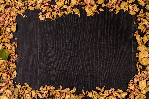 Pilha de rosas secas em fundo preto de madeira como borda.
