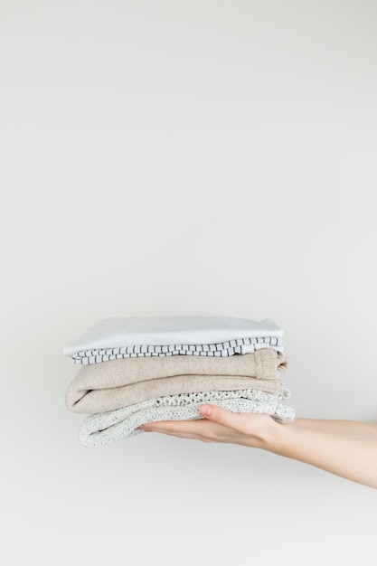 Pilha de roupas nas mãos femininas. Roupa ordenadamente empilhada no fundo branco e no copyspace vertical.